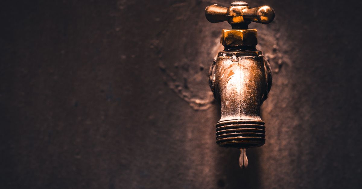 a close up view of a vintage brass faucet with a single water droplet against a dark background